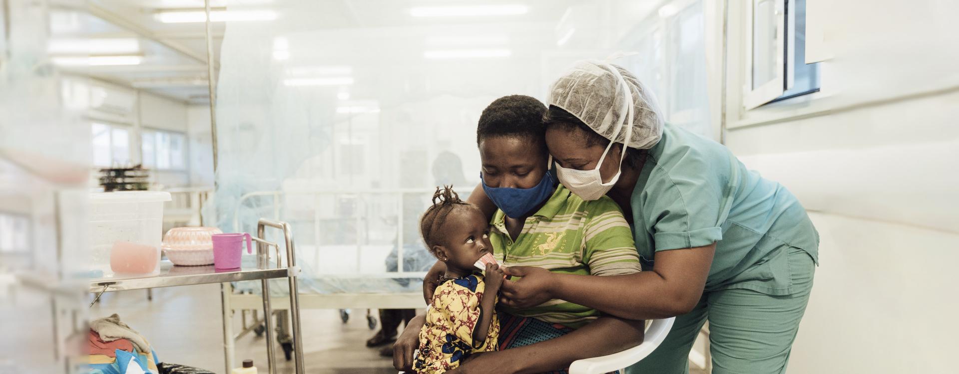  Christiana Musa, enfermera de MSF, y la madre Mariama Kamara, dan comida terapéutica lista para usar a la pequeña Alice Tilu. 