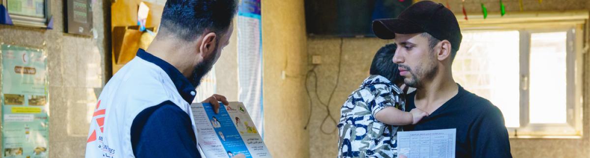 Un promotor de salud de MSF habla con un padre que lleva a su hijo en brazos en el centro de salud Mustafa Al-Adhari, en Sadr City, Bagdad.