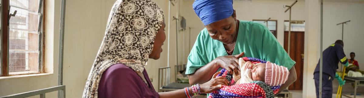 La auxiliar de enfermería Ndayumvire Antoinette sostiene a un bebé mientras habla con la madre en la sala de maternidad del hospital de Médicos Sin Fronteras del campamento de Nduta.