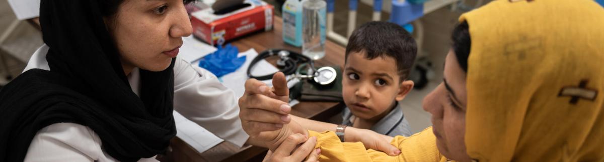 En la clínica Mehr, situada al suroeste de Teherán gestionada por MSF, un médico toma la tensión arterial a una madre que ha acudido a la clínica con su hijo pequeño.