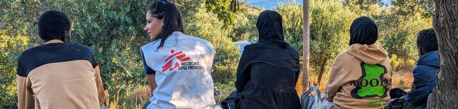 Una persona del equipo de MSF sentada con un grupo de personas recién llegadas a la isla griega de Lesbos, que descansan tras ser atendidas por los equipos de MSF y recibir alimentos y agua.