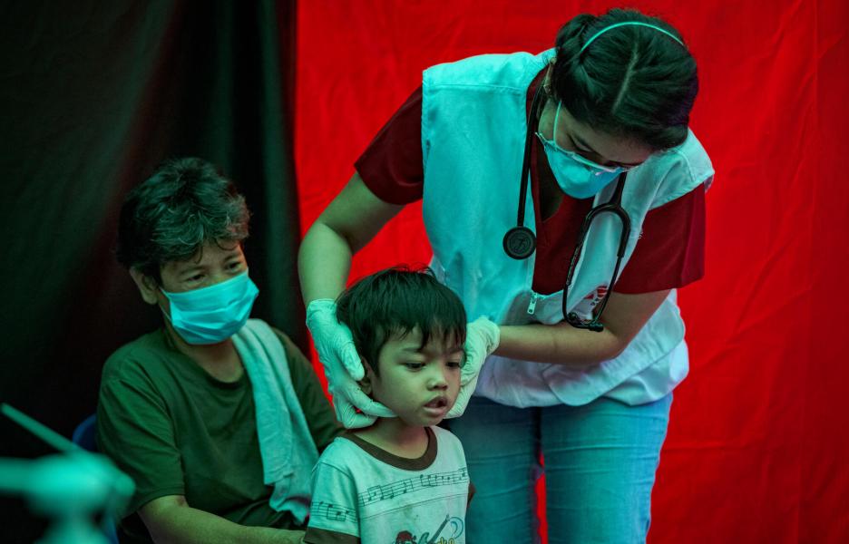 Agustina observa cómo Trisha Thadhani, médica especialista en tuberculosis de MSF, realiza una evaluación médica a su nieto Ion en uno de los centros de detección activa de tuberculosis de MSF el 13 de marzo de 2023 en Tondo, Manila, Filipinas.