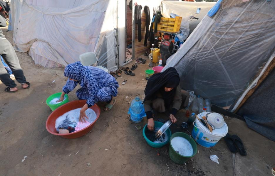 Mujeres palestinas desplazadas lavan ropa y vajilla en cubos frente a sus tiendas de campaña en el barrio de Al-Shaboura, en la ciudad de Rafah, al sur de Gaza, el 27 de enero de 2024.