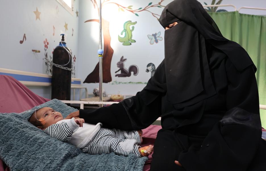 Salwa sentada en la cama de su nieto en el hospital materno-infantil Al-Qanauis de MSF.