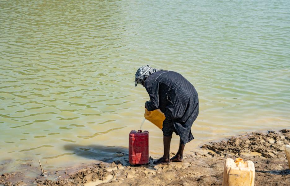 Un anciano recoge agua con bidones de un estanque en Atam.