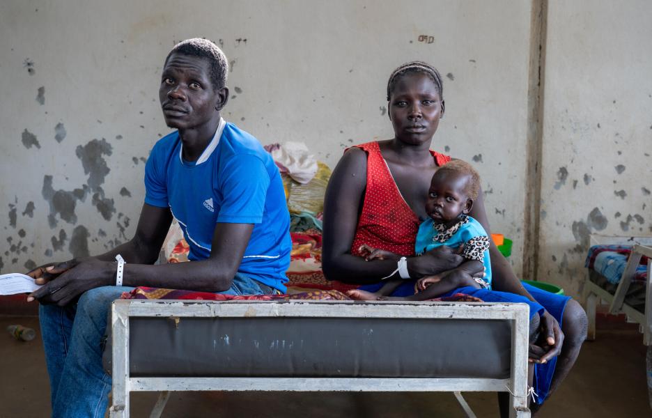 Una madre y un padre sentados junto a su hijo Una madre y un padre sentados junto a su hijo, que recibe tratamiento en el campo de Kulé