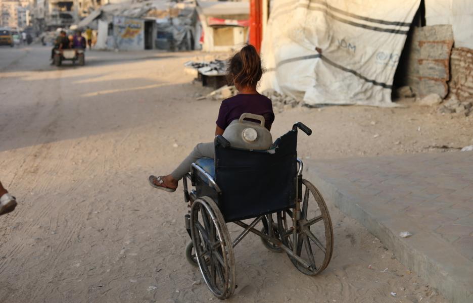 Una niña sentada en una silla de ruedas que utiliza para transportar bidones de agua.