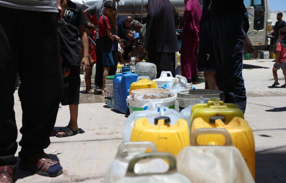 Personas desplazadas en Gaza alinean sus bidones vacíos esperando el reparto de agua.