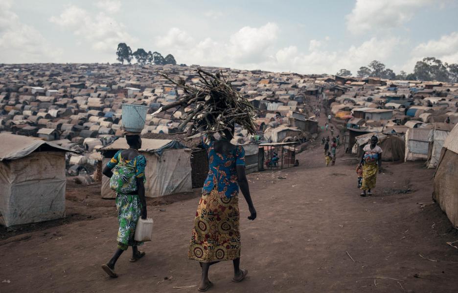 Unas mujeres caminan por el campamento de desplazados de Plaine Savo, cargando leña y agua. El campamento, situado cerca de Fataki, acoge a unas 76 000 personas desplazadas.