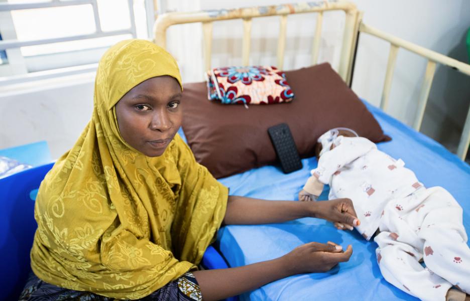 Nusaiba Al Mustapha, de 27 años, está sentada junto a su hijo de 19 meses, Umar Kasim, mientras este recibe tratamiento contra la desnutrición.