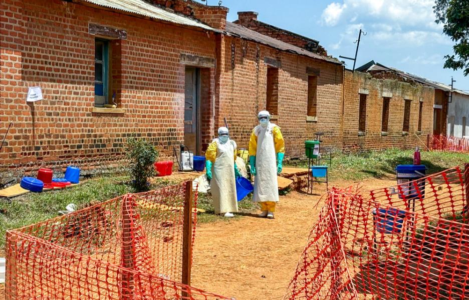 Dos profesionales sanitarios, equipados con equipo de protección individual (EPI), se encuentran frente a las salas donde se atiende a los pacientes con ébola en el centro de tratamiento del ébola de Médicos Sin Fronteras, en el Hospital General de Referencia de Bambu.