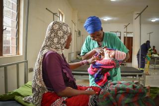La auxiliar de enfermería Ndayumvire Antoinette sostiene a un bebé mientras habla con la madre en la sala de maternidad del hospital de Médicos Sin Fronteras del campamento de Nduta.