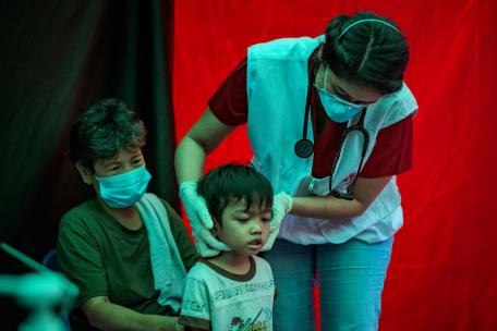 Agustina observa cómo Trisha Thadhani, médica especialista en tuberculosis de MSF, realiza una evaluación médica a su nieto Ion en uno de los centros de detección activa de tuberculosis de MSF el 13 de marzo de 2023 en Tondo, Manila, Filipinas.