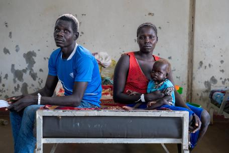 Una madre y un padre sentados junto a su hijo Una madre y un padre sentados junto a su hijo, que recibe tratamiento en el campo de Kulé