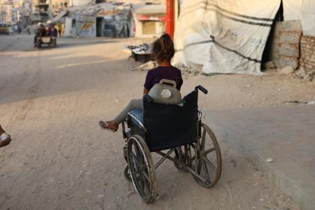 Una niña sentada en una silla de ruedas que utiliza para transportar bidones de agua.