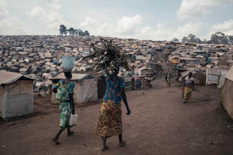 Unas mujeres caminan por el campamento de desplazados de Plaine Savo, cargando leña y agua. El campamento, situado cerca de Fataki, acoge a unas 76 000 personas desplazadas.