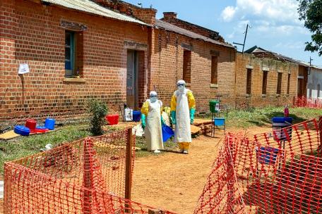 Dos profesionales sanitarios, equipados con equipo de protección individual (EPI), se encuentran frente a las salas donde se atiende a los pacientes con ébola en el centro de tratamiento del ébola de Médicos Sin Fronteras, en el Hospital General de Referencia de Bambu.
